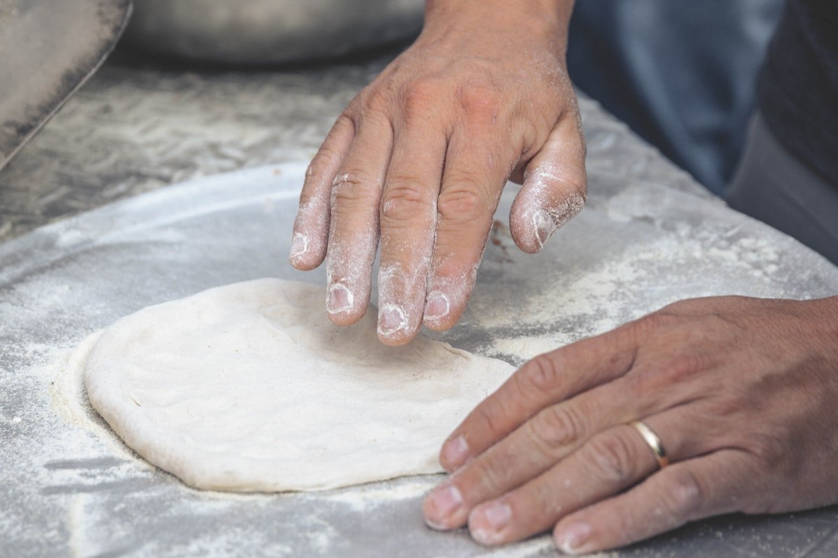Person holding pizza dough stretched on a metal pizza peel