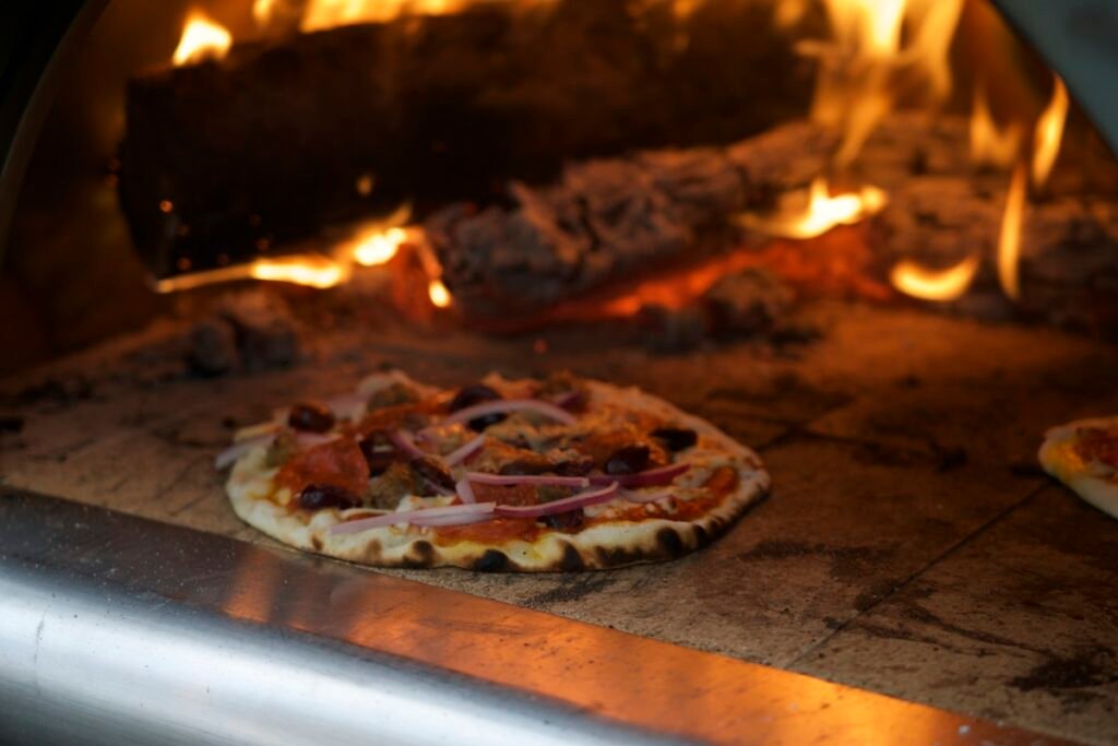 Pizza cooking inside a wood-fired oven with flames