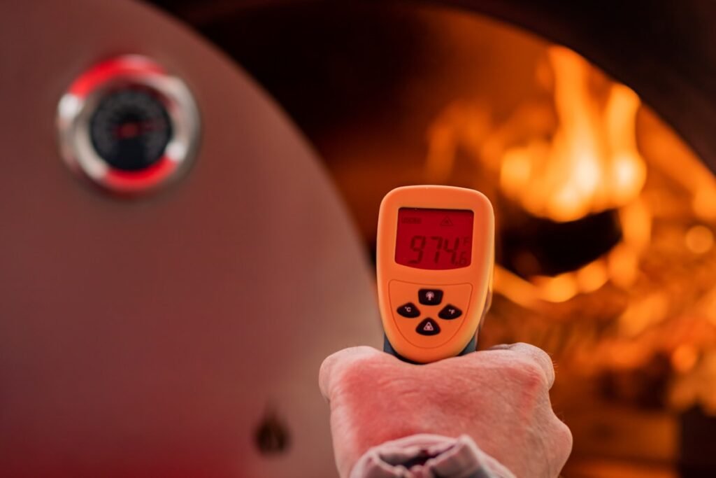 Best Infrared Thermometers for Pizza Ovens Person pointing an infrared thermometer at a fire in a pizza oven